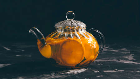 Glass teapot with tea from orange and herbs on a wooden table.の写真素材