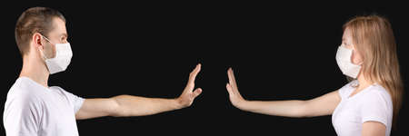 A man and a woman in medical masks stand opposite each other with their arms outstretched against a...