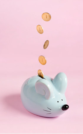 blue piggy bank in the form of a mouse with falling coins on a pink background, studio shot, artificial lightの写真素材