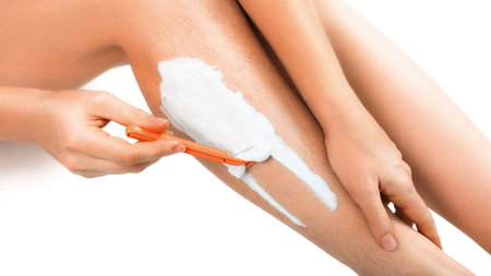 A girl shaves a leg with long hair with a shaving machine with shaving foam close-up.の写真素材