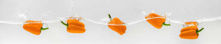 Beautiful orange sweet peppers fall into the water with splashes on a white background, healthy vegetarian foodの写真素材