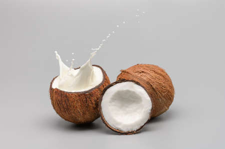 Whole and broken in half coconut with a splash of coconut milk on a gray background close-upの写真素材