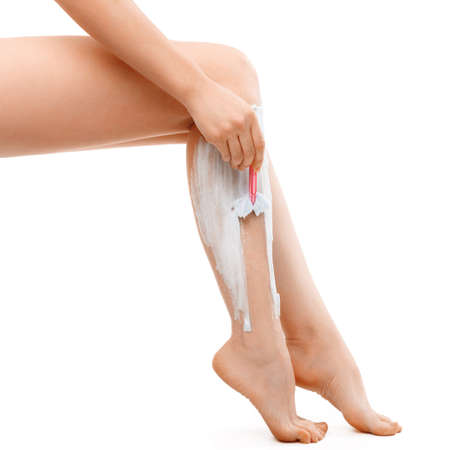 A girl sitting shaves her legs with a shaving machine with shaving foam on a white isolated backgroundの写真素材