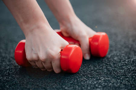 The girl is holding red dumbbells lying on a rubberized sports field. The concept of fitness, sports or athletics.の写真素材