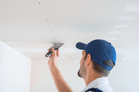 A master in uniform puts putty on the caps of self-tapping screws for fixing plasterboard sheets on the ceiling.の写真素材
