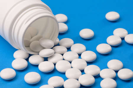 A handful of white tablets or vitamins or nutritional supplements poured out of a white bubble on a blue uniform background.の写真素材