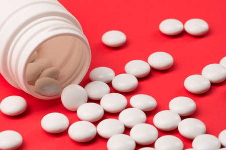 A handful of white tablets or vitamins or food additives poured out of a white bubble on a red uniform background.の写真素材