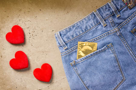 Blue jeans with a condom in a pocket and three hearts on a stone backgroundの写真素材