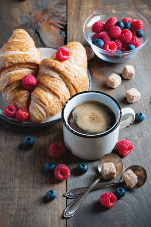 Coffee and croissants with raspberries and fruits for breakfast. Enamel mug. Toned image, selective focusの写真素材