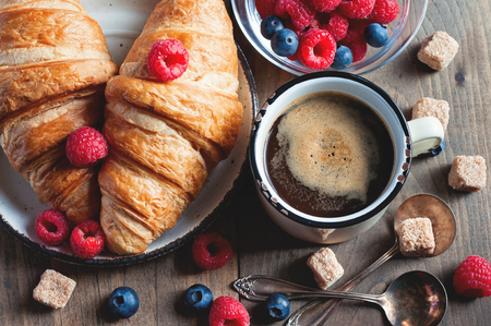 Coffee and croissants with raspberries and fruits for breakfast. Toned image, selective focusの写真素材