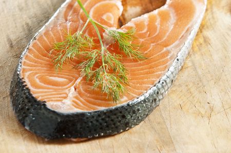 Raw salmon fillet garnished with dill on an old wooden kitchen boardの写真素材