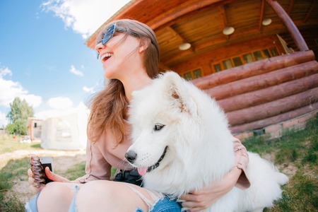 young stylish hipster woman girl playing white kid-skin dog in country side, village wood house,...