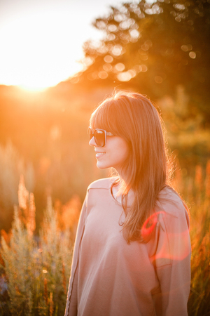 Portrait of young modern girl on the background of nature. Young woman  on a background sunset. Young woman in ripped jeans. in sun glassesの写真素材