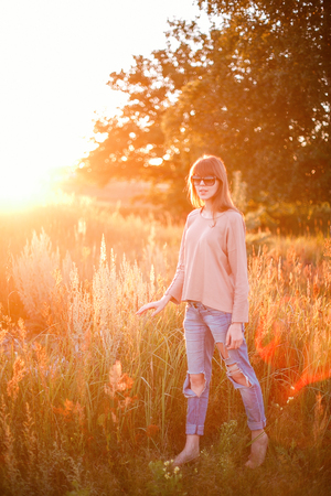 Portrait of young modern girl on the background of nature. Young woman  on a background sunset. Young woman in ripped jeans. in sun glassesの写真素材