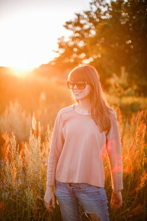 Portrait of young modern girl on the background of nature. Young woman  on a background sunset. Young woman in ripped jeans. in sun glassesの写真素材