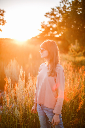 Portrait of young modern girl on the background of nature. Young woman  on a background sunset. Young woman in ripped jeans. in sun glassesの写真素材