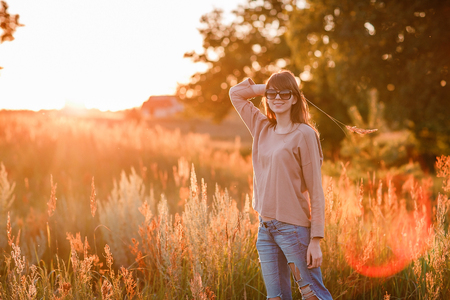 Portrait of young modern girl on the background of nature. Young woman  on a background sunset. Young woman in ripped jeans. in sun glassesの写真素材