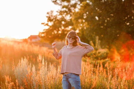 Portrait of young modern girl on the background of nature. Young woman  on a background sunset. Young woman in ripped jeans. in sun glassesの写真素材
