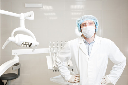 dentist standing in the dental office and looking at camera. in the mask, glasses, a white coatの写真素材