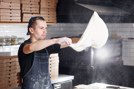 Roll out the dough. expanding cloud of flour. Closeup hand of chef baker in uniform blue apron cook pizza at kitchenの写真素材