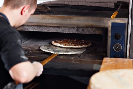 Raw pizza ready to Bake in the oven. Cook in a blue apron in the kitchen. with a shovel in his hands.の写真素材