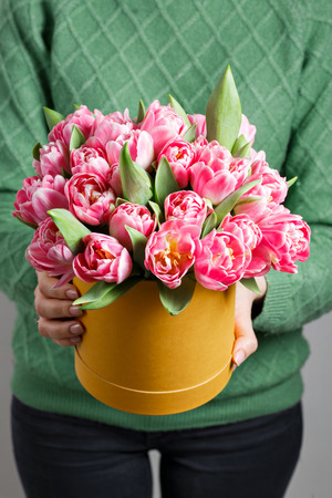 Young beautiful woman holding a bouquet of tulips in a gift box. pink colors in one box or bouquet. Present on March 8 or other celebration.の写真素材