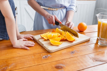 Mom cuts fruit to her son. sliced oranges on a wooden cutting board. Healthy and tasty breakfastの写真素材