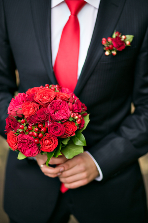 groom holding bridal bouquet close up. red garden roses decorated in compositionの写真素材