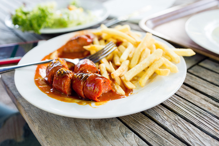 Snacks to beer on a white plate. Bavarian fried sausages, fried potatoes, chips on a wooden table background.の写真素材