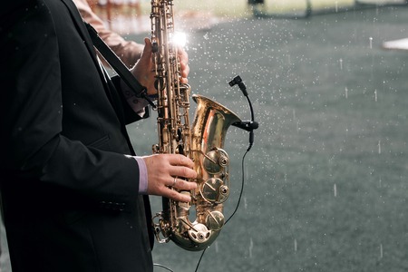 Man with a saxophone stands under rainの写真素材
