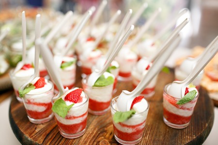 Pink coloured strawberry dessert in shot glass, decorated with mint leaves, on wood plate, several strawberries at background. catering buffetの写真素材