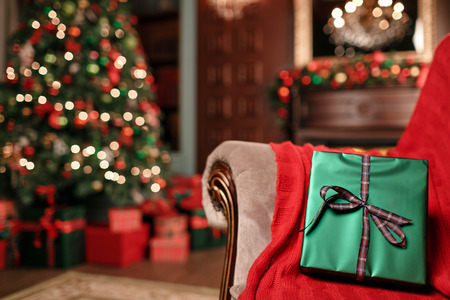 Green christmas gift close-up on foreground. Bow of red ribbon. Abstract background with blurred lights and tree. copy spaceの写真素材