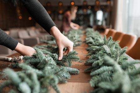 Florist at work: woman hands making christmas decorations garland of fir. Happy new year dinner feastの写真素材