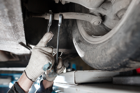 Car mechanic examining car suspension of lifted automobile at repair service stationの写真素材