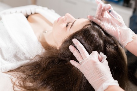 Handsome woman receives an injection in the head. The procedure makes doctor in white gloves. The concept of mesotherapy. Thrust to strengthen the hair and their growthの写真素材