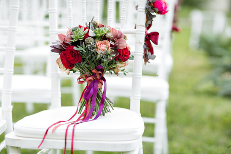 Stunning red bridal bouquet on white chair. Wedding ceremony. Mix of succulents, orchids and rosesの写真素材