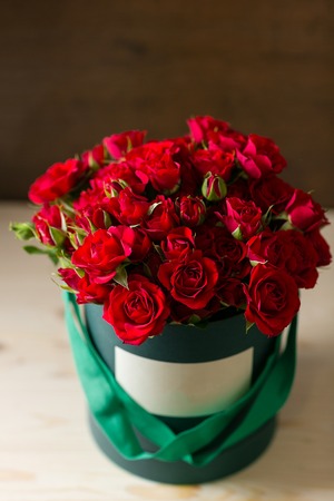 Bouquet of red spray roses in a box on wooden table. copy space. blank for textの写真素材