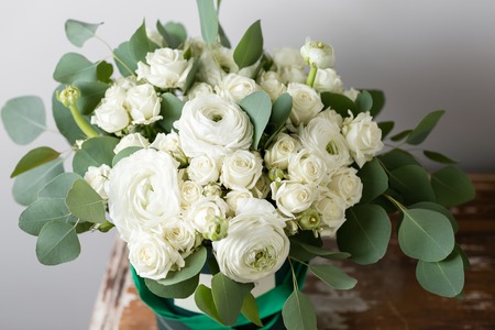 Mixed white flowers . Bouquet of spray roses and ranunculuses in a box on wooden table. copy space.