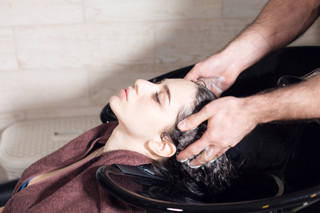 beautiful girl washes her hair before a haircut in a beauty salon. hair washing at a hairdressing, young caucasian girl. professional shampoo. stylist hairdresser manの写真素材
