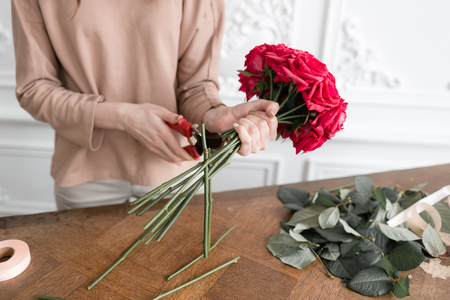 Young woman florist arranging plants in flower shop. People, business, sale and floristry concept. Bouquet of red rosesの写真素材