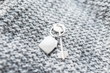 House key and keychain in the form of homes lies on knitted wool fabric. Concept for real estate,...