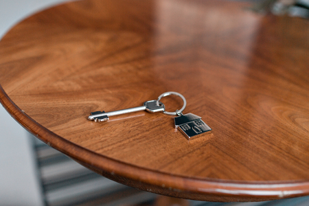 House key and keychain in the form of homes lies on wooden table. Concept for real estate, mortgage, moving home or renting property.の写真素材