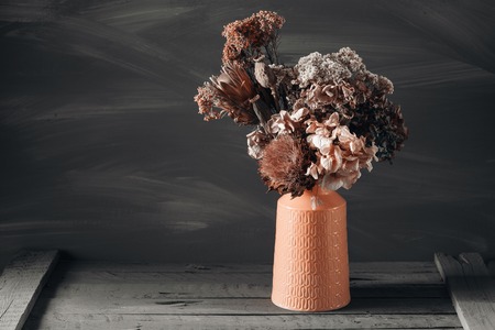 Still life image of dried flowers in rustic vase against weathered wooden backgroundの写真素材