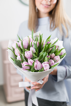 Sunny spring morning. Young happy woman holding a beautiful bunch of lilac tulips in her hands. Present for a smiles girl. Flowers bouquet in headboxの写真素材
