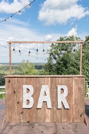Simple bar concept. Summer cafe on terrace with vintage wooden furniture on background blue sky. Alcoholic catering serviceの写真素材