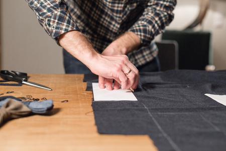 Cutting dark wool fabric. the line pattern. Young man working as a tailor and using a sewing machine...
