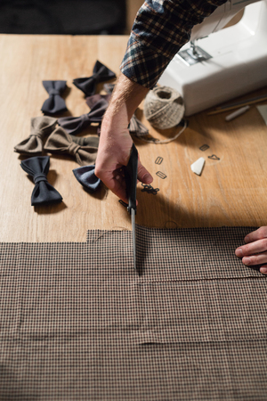 Closeup cutting brown plaid wool fabric. the line pattern. Young man working as a tailor and using a sewing machine in workshop.の写真素材