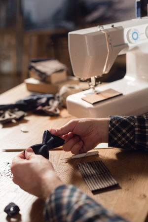 Close-up creates the shape of a butterfly tie made of wool. Good looking young man working as a tailor and using a sewing machine in a textile studio.の写真素材