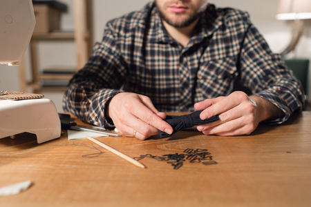 with a needle and thread in hand. Good looking young man working as a tailor and using a sewing machine in a textile studio.の写真素材