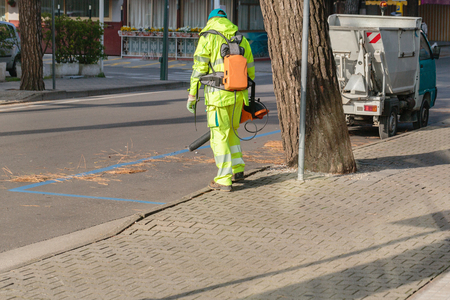 Landscaper worker cleaning foot way in park from dead leaves. Using electric powered Leaf Blowerの写真素材